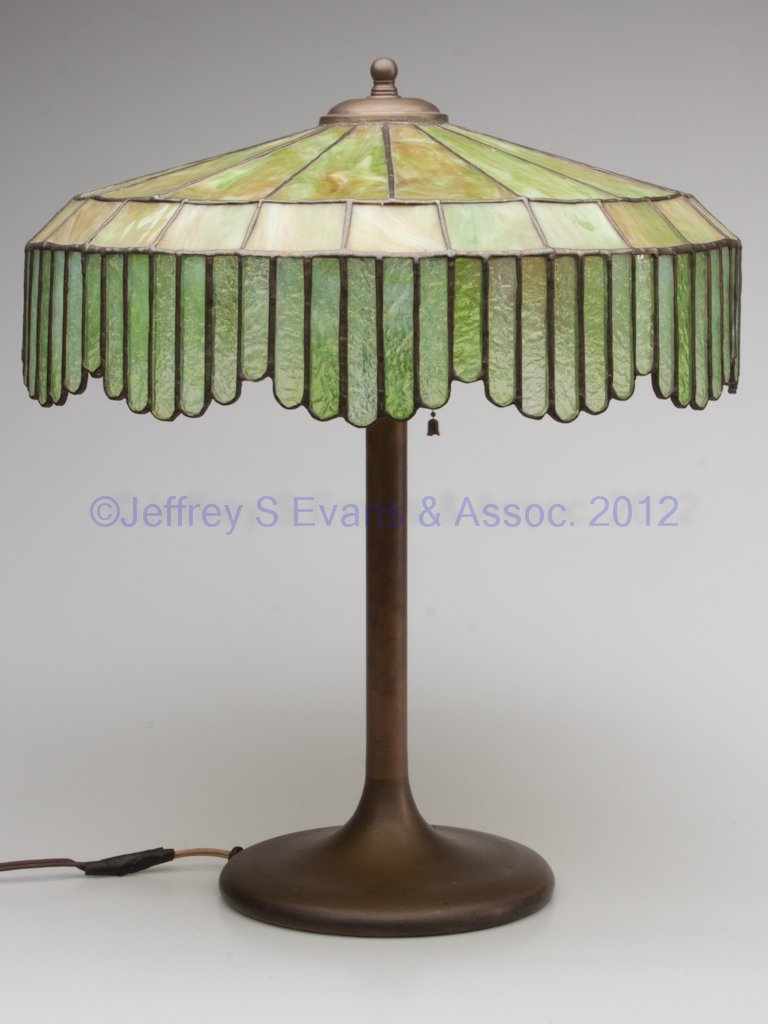 ARTS & CRAFTS LEADED-GLASS SHADE TABLE LAMP: ARTS & CRAFTS LEADED-GLASS SHADE TABLE LAMP, shade with green slag and textured opalescent glass insets, raised on a brass base. No markings located. First half 20th century. 20" HOA, 16 1/2" D shade.