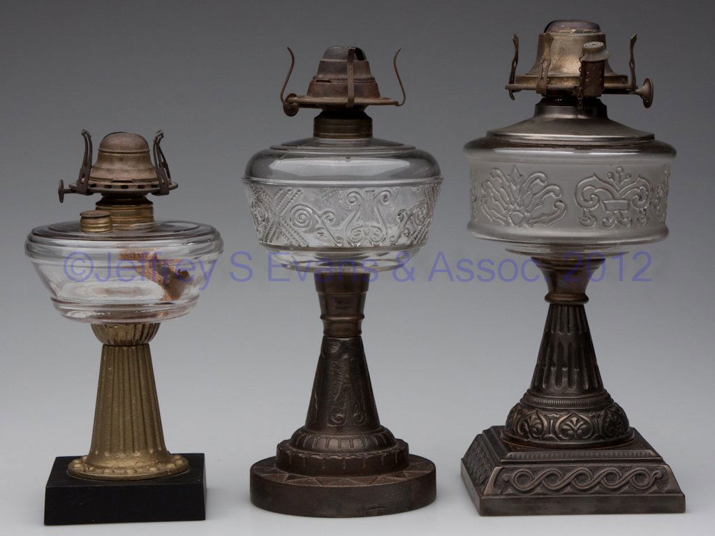 ASSORTED COMPOSITE KEROSENE STAND LAMPS, LOT OF TH: ASSORTED COMPOSITE KEROSENE STAND LAMPS, LOT OF THREE, glass fonts raised on cast-iron bases, small font embossed with Barries Patent 1875 and with shoulder filler, each with burner. Fourth quarter 19
