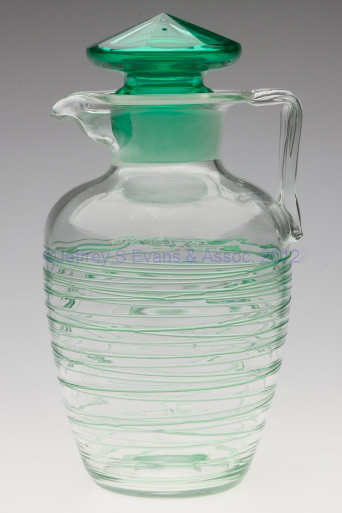 STEUBEN REEDED COCKTAIL SHAKER: STEUBEN REEDED COCKTAIL SHAKER, colorless with green applied random reeding, shape 7056, light rib-optic, applied strap handle, original green stopper, polished pontil mark. Steuben Glass Works. Circa
