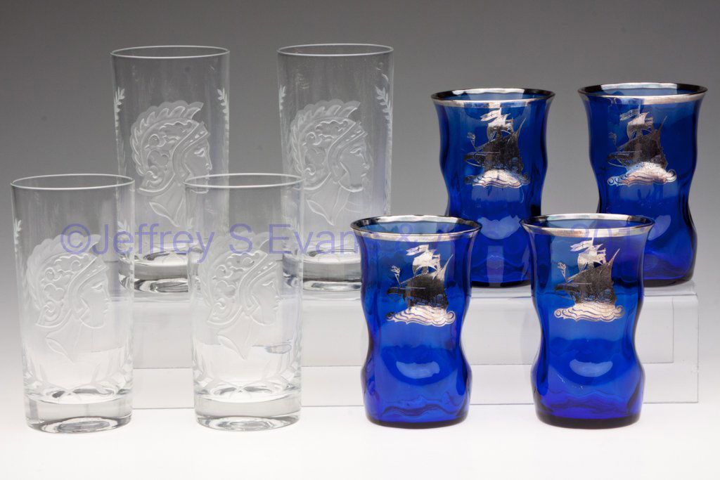DECORATED GLASS TUMBLERS, TWO SETS OF FOUR: DECORATED GLASS TUMBLERS, TWO SETS OF FOUR, comprising a cobalt blue set with pinched sides and silver overlay Spanish galleon decoration, and a colorless set with intaglio carved Trojan warrior heads
