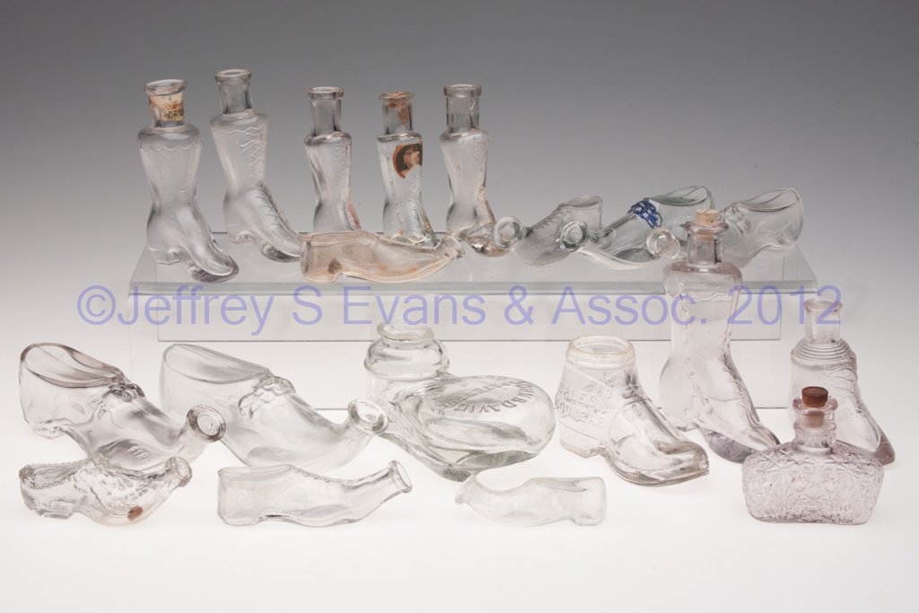 ASSORTED GLASS FIGURAL SHOES / BOOT BOTTLES, LOT O: ASSORTED GLASS FIGURAL SHOES / BOOT BOTTLES, LOT OF 19, colorless, comprising two inkwells, the remainder probably for perfume. Late 19th/early 20th century. 1" to 4 1/4" H. Provenance: From a Michiga