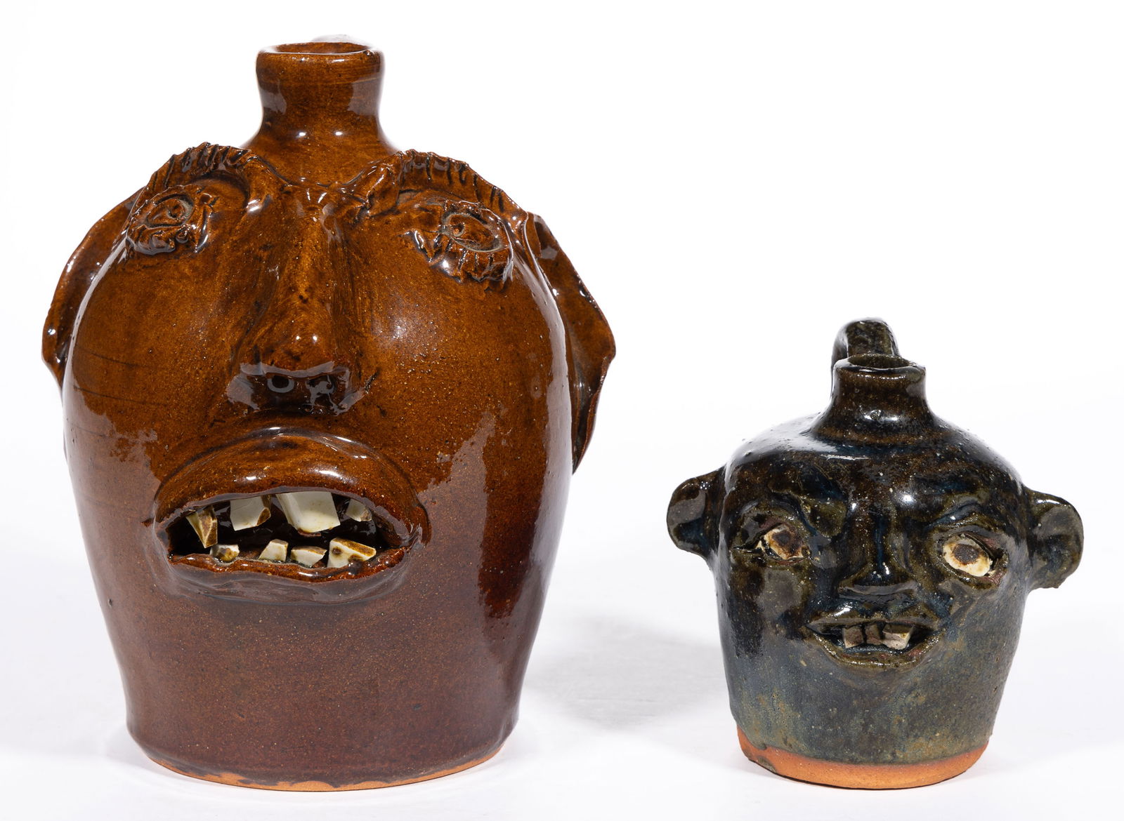 GEORGIA / NORTH CAROLINA EARTHENWARE / REDWARE FACE JUGS, LOT OF TWO: GEORGIA / NORTH CAROLINA EARTHENWARE / REDWARE FACE JUGS, LOT OF TWO, each having molded features including eyes, a pinched nose, puckered lips with inset china teeth, protruding ears, and a