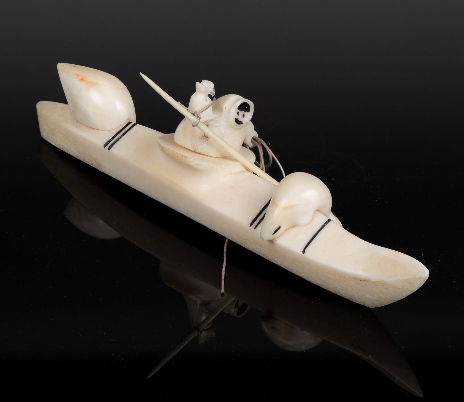 JUSTIN TIULANA (ALASKAN INUPIAQ, B. C. 1947) NATIVE AMERICAN HUNTER CARVED BONE FIGURE: JUSTIN TIULANA (ALASKAN INUPIAQ, B. C. 1947) NATIVE AMERICAN HUNTER CARVED BONE FIGURE, depicting a hunter in a kayak, raising a spear in one hand and holding onto the connecting rope in the other, ai