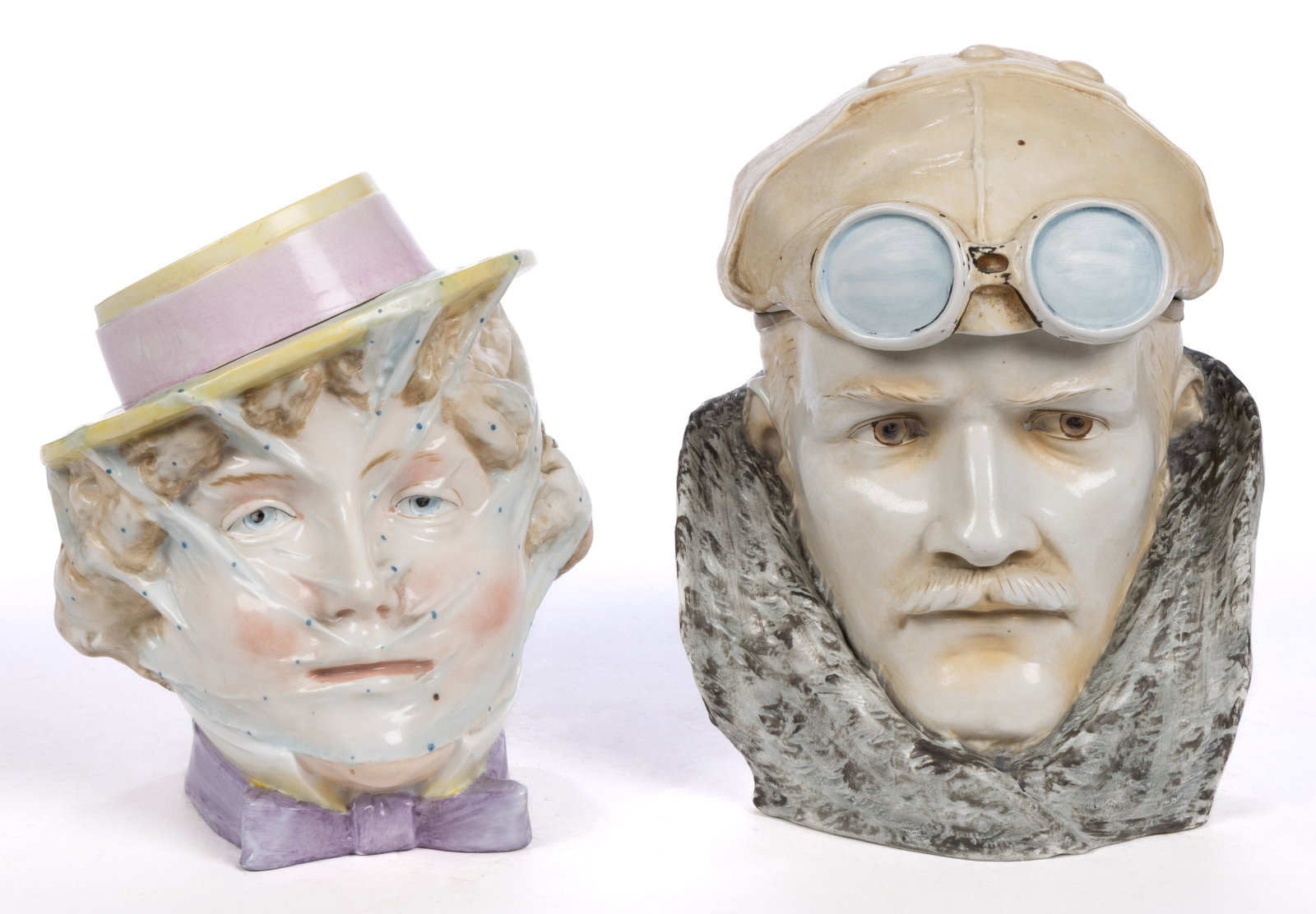 GERMAN PORCELAIN FIGURAL MOTORIST HEAD HUMIDORS, LOT OF TWO: GERMAN PORCELAIN FIGURAL MOTORIST HEAD HUMIDORS, LOT OF TWO, each polychrome hand-painted, comprising a handsome mustached gentleman with leather cap and motoring goggles and a young woman wearing a f