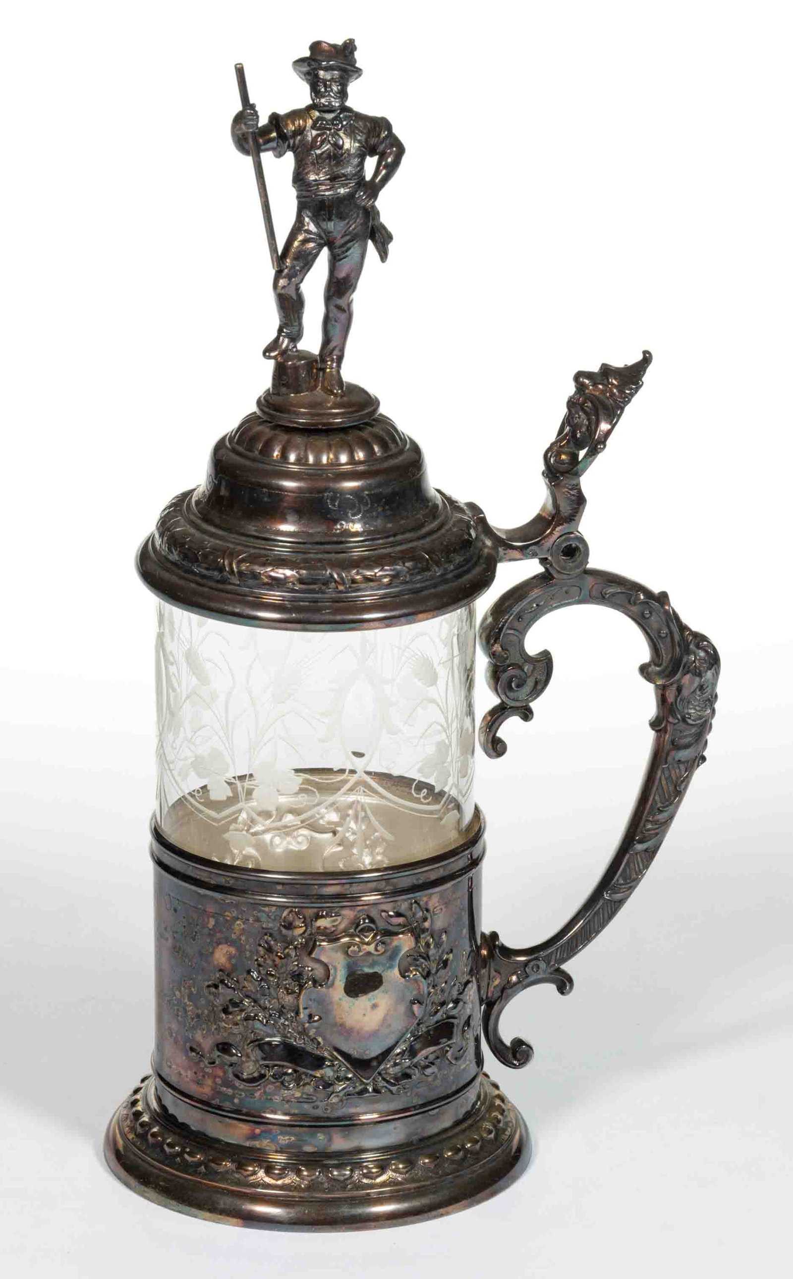 EUROPEAN BLOWN AND ENGRAVED GLASS STEIN: EUROPEAN BLOWN AND ENGRAVED GLASS STEIN, colorless, cylindrical insert with scrolling wheat/hops decoration fitted into a silver-plate frame and mount with the base featuring shields resting of a bed 