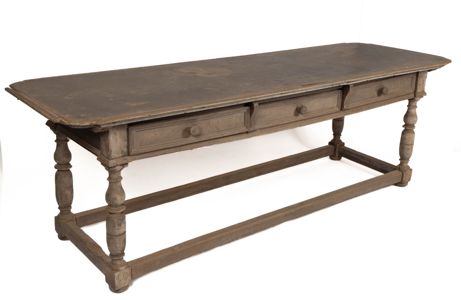 AMERICAN COLONIAL-STYLE STRETCHER-BASE TAVERN TABLE: AMERICAN COLONIAL-STYLE STRETCHER-BASE TAVERN TABLE, walnut, featuring a rectangular top with shaped corners resting on a base with three drawers with turned knobs, the whole resting on a four turned 