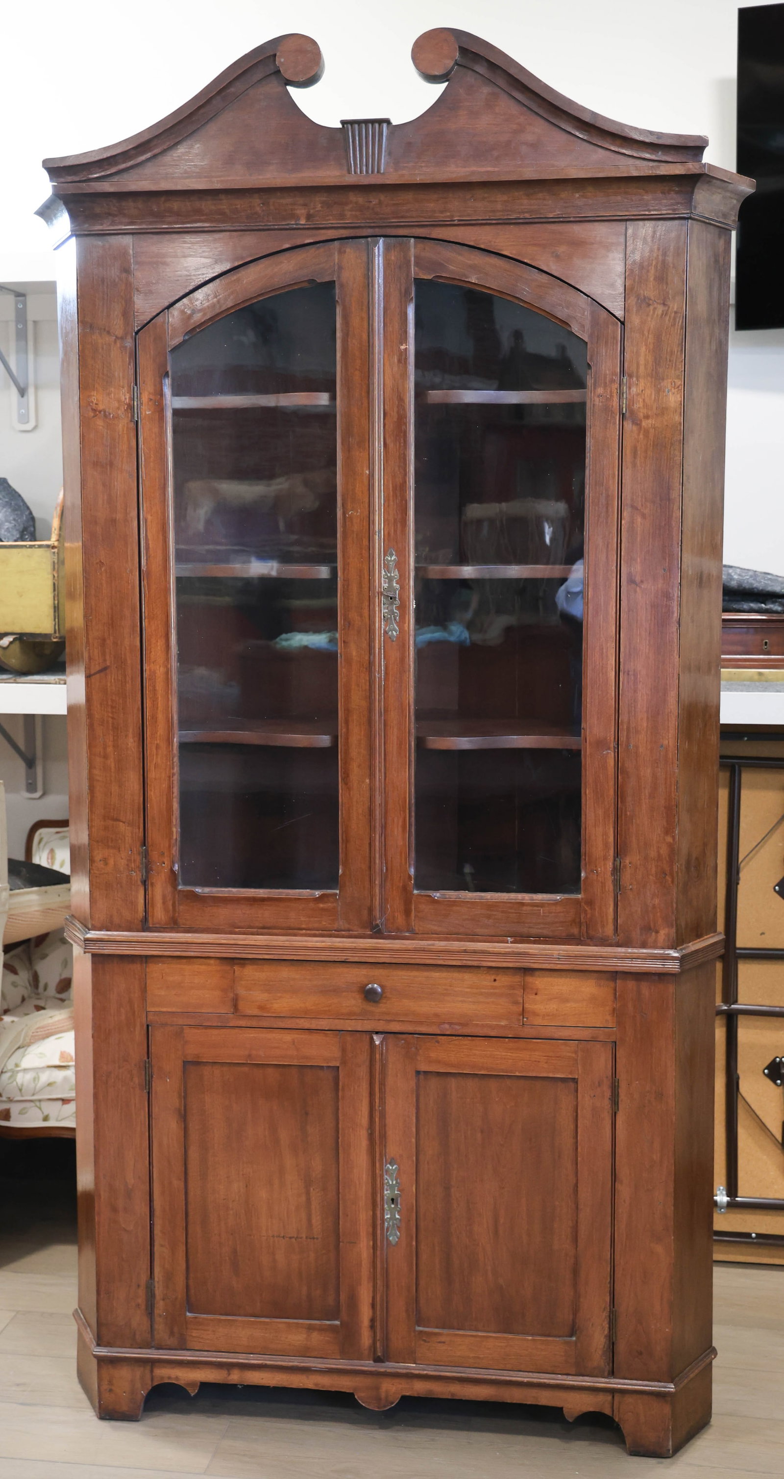 MID-ATLANTIC WALNUT CORNER CUPBOARD: MID-ATLANTIC WALNUT CORNER CUPBOARD, two-piece construction, features a broken arch cornice above two arched single-pane glass doors, the base with one center drawer and two fielded panel cabinet door