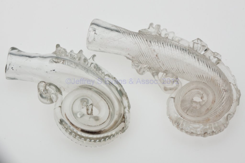 BLOWN DOLPHIN OR MERMAID PUNGENTS, LOT OF TWO: BLOWN DOLPHIN OR MERMAID PUNGENTS, LOT OF TWO, colorless, one molded with tiny swirled ribs, each with applied rigaree to sides, plain mouth, and rough pontil scar on end. Boston & Sandwich Glass Co. 