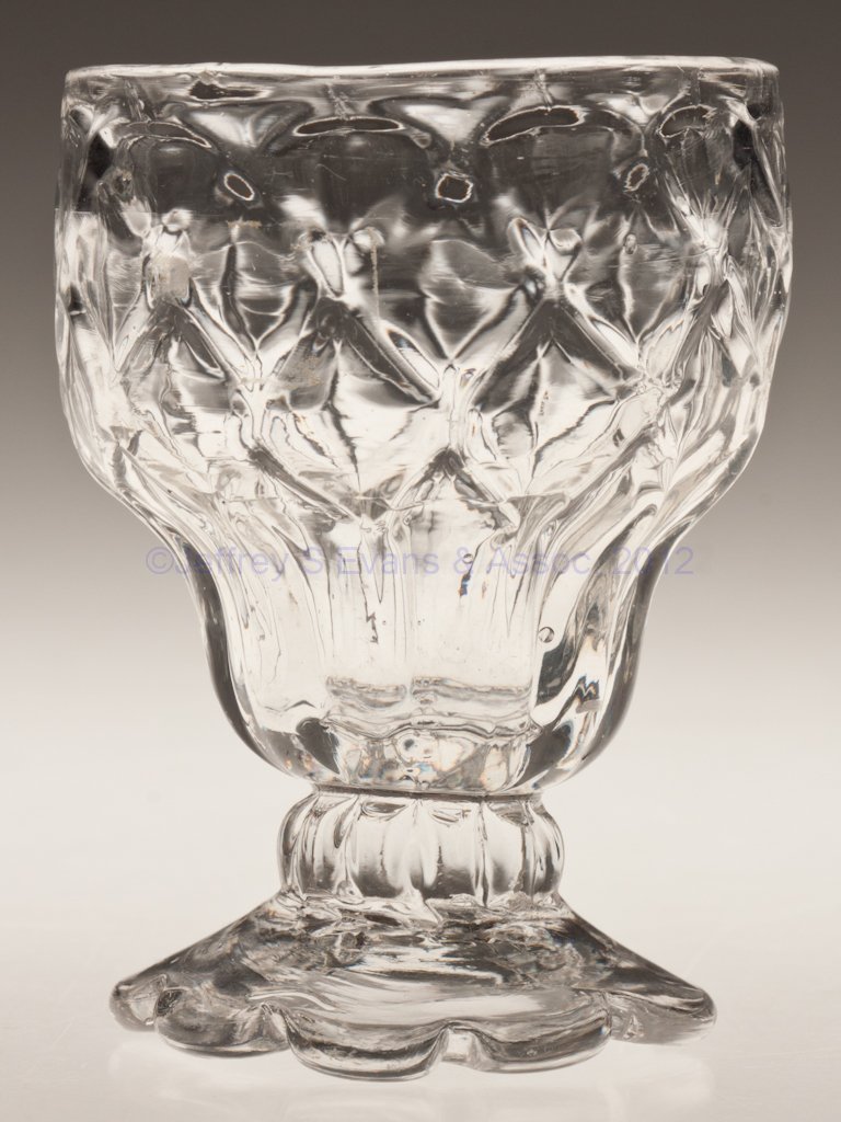 PATTERN-MOLDED FOOTED SALT: PATTERN-MOLDED FOOTED SALT, colorless, double-ogee body molded with four complete rows of 11 diamonds, raised on a short 11-rib stem and sloping seven-petal foot with rough iron pontil mark. Possibly 