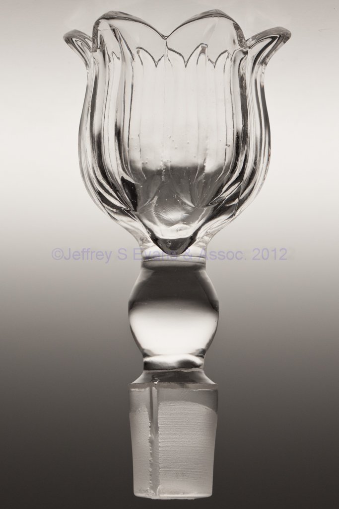 MAGNET AND GRAPE WITH FROSTED LEAF DISPENSER STOPP: MAGNET AND GRAPE WITH FROSTED LEAF DISPENSER STOPPER, colorless lead glass, with air-intake groove to side of extension. Third quarter 19th century. 5 1/2" LOA, 1 1/8" D of extension at shoulder. Prov