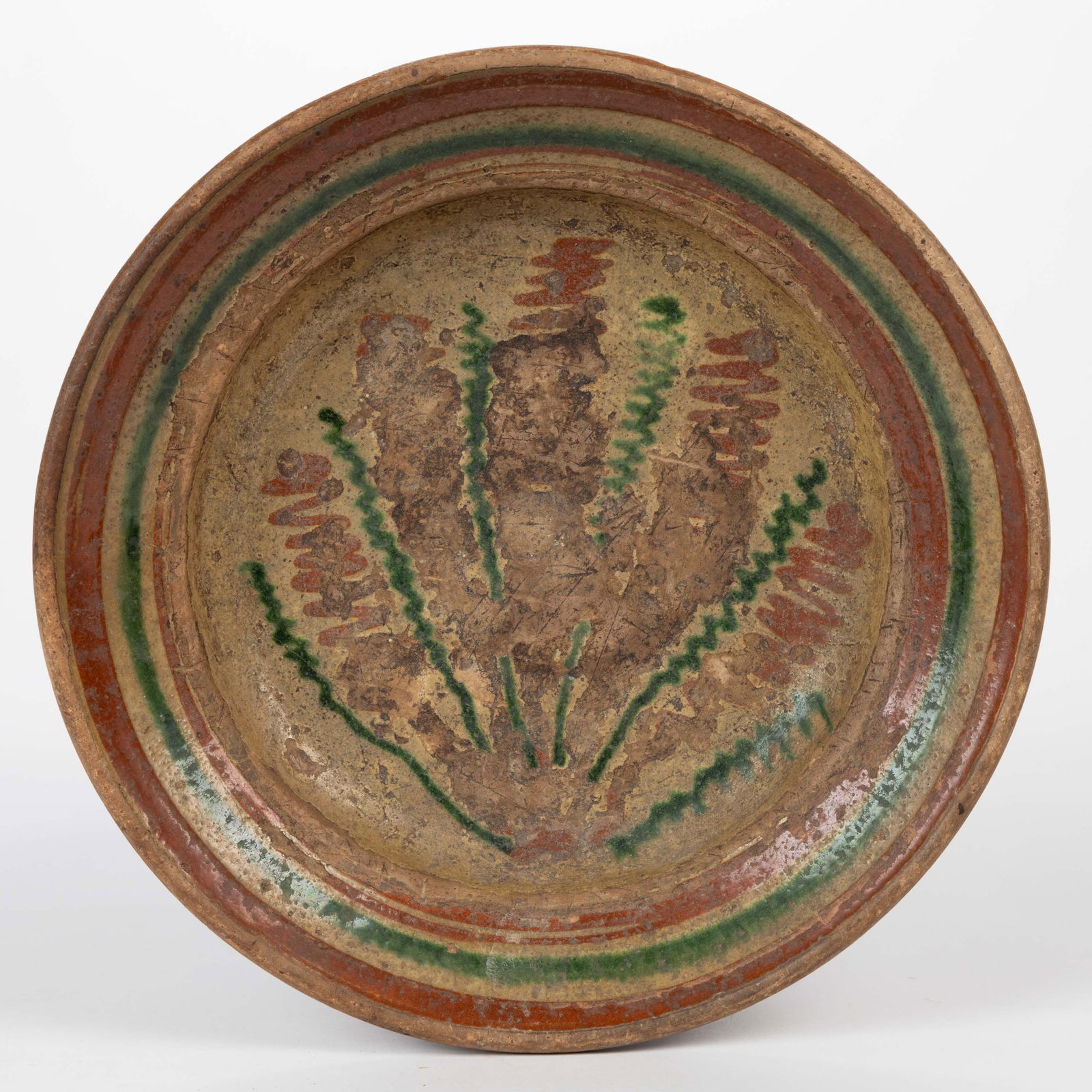 SALEM, NORTH CAROLINA MORAVIAN POLYCHROME-DECORATED EARTHENWARE / REDWARE DISH / PLATE: SALEM, NORTH CAROLINA MORAVIAN POLYCHROME-DECORATED EARTHENWARE / REDWARE DISH / PLATE, single lead-glazed, interior featuring a stylized plant design of copper- and brown-slip on white slip base. Pos