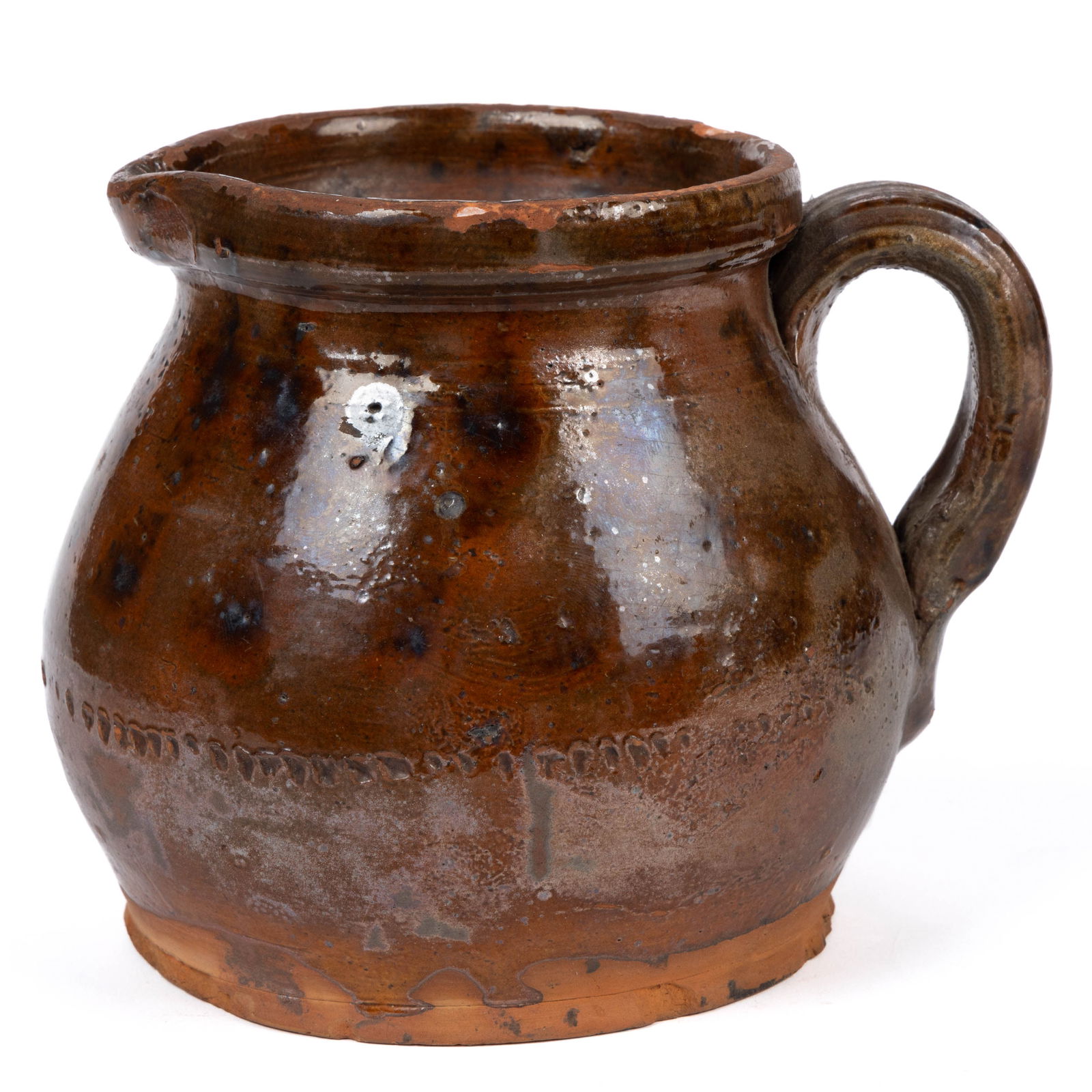 AMERICAN DECORATED EARTHENWARE / REDWARE BATTER PITCHER: AMERICAN DECORATED EARTHENWARE / REDWARE BATTER PITCHER, lead- and manganese-glazed, squat ovoid form with galleried rim, a crude coggled ring in line with the lower handle terminal, and lig