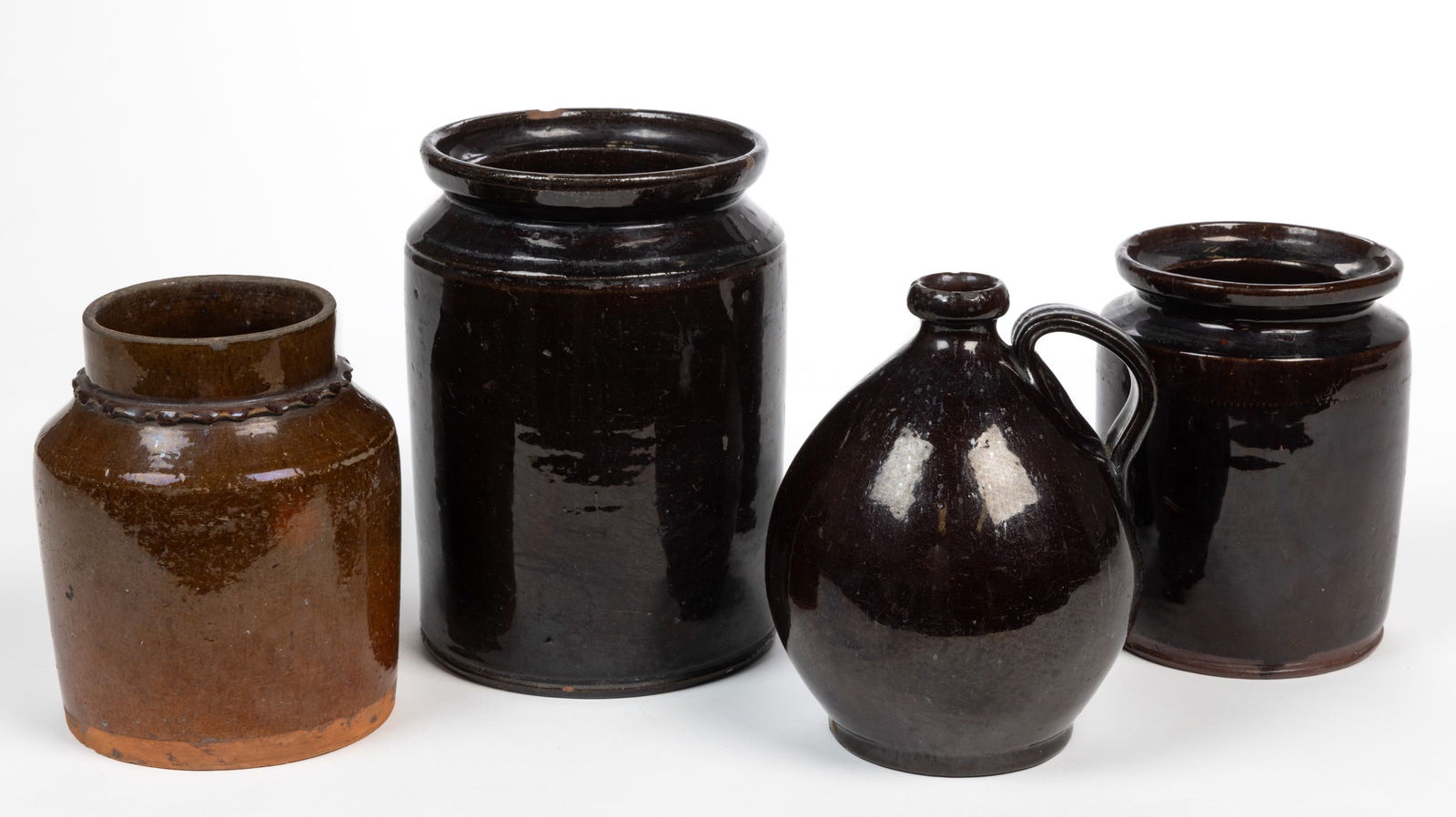 AMERICAN EARTHENWARE / REDWARE ARTICLES, LOT OF FOUR: AMERICAN EARTHENWARE / REDWARE ARTICLES, LOT OF FOUR, lead-glazed, comprising one ovoid jug with applied strap handle and three jars of cylindrical form including one having applied neck ruf