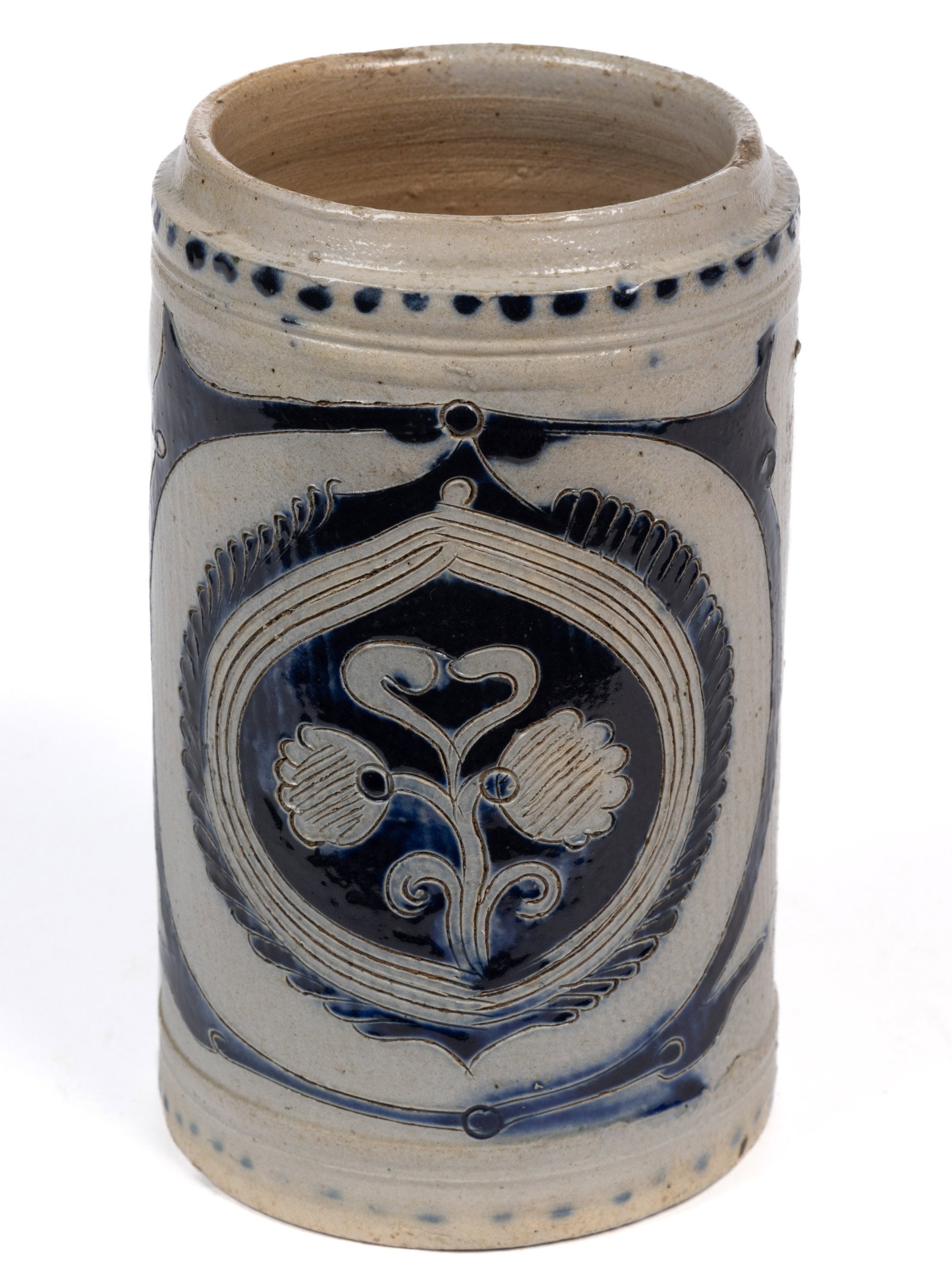 GERMAN WESTERWALD DECORATED STONEWARE MUG: GERMAN WESTERWALD DECORATED STONEWARE MUG, salt-glazed, cylindrical form with applied strap handle and hole to top, featuring incised double-bloom stylized floral design to front with cobalt deco