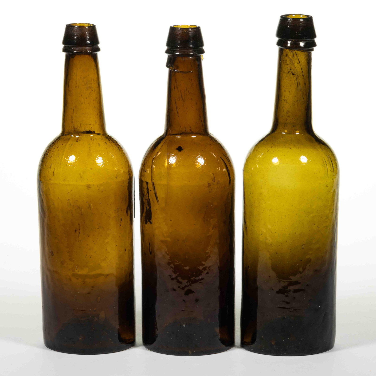 AMERICAN CYLINDER WHISKEY BOTTLES, LOT OF THREE: AMERICAN CYLINDER WHISKEY BOTTLES, LOT OF THREE, colors varying between olive-amber and brighter yellow-amber, tall cylindrical forms, blown in three-piece molds with shoulder seams visible, applied d