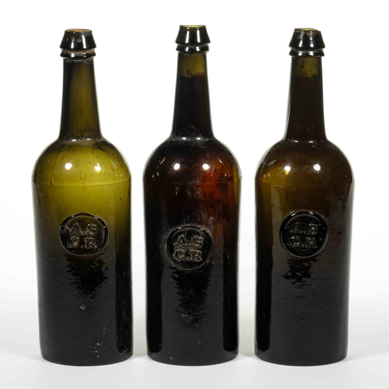 ENGLISH ALL SOULS COMMON ROOM APPLIED SEAL BLACK GLASS WINE BOTTLES, LOT OF THREE: ENGLISH ALL SOULS COMMON ROOM APPLIED SEAL BLACK GLASS WINE BOTTLES, LOT OF THREE, very dark olive green/black, tall cylindrical form blown in an unmarked Ricketts-style three-piece mold, applied roun
