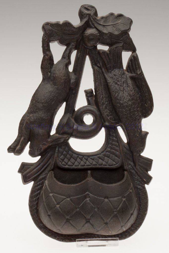 CAST IRON FIGURAL WALL-MOUNT MATCH HOLDER: CAST IRON FIGURAL WALL-MOUNT MATCH HOLDER, depicting a hunter's pouch with two open compartments below a striker panel, horn between a hanging rabbit and bird, reverse impressed "PAT'D SEPT 27 / 1870"