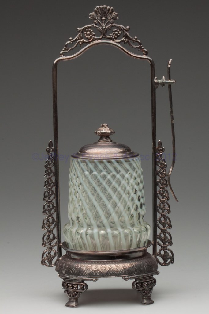 CHRYSANTHEMUM SWIRL PICKLE CASTER: CHRYSANTHEMUM SWIRL PICKLE CASTER, colorless opalescent, Rockford #660 quadruple-plate stand with fork. Fourth quarter 19th century. 11" HOA, 4" H jar. Provenance: From the collection of the late Marj