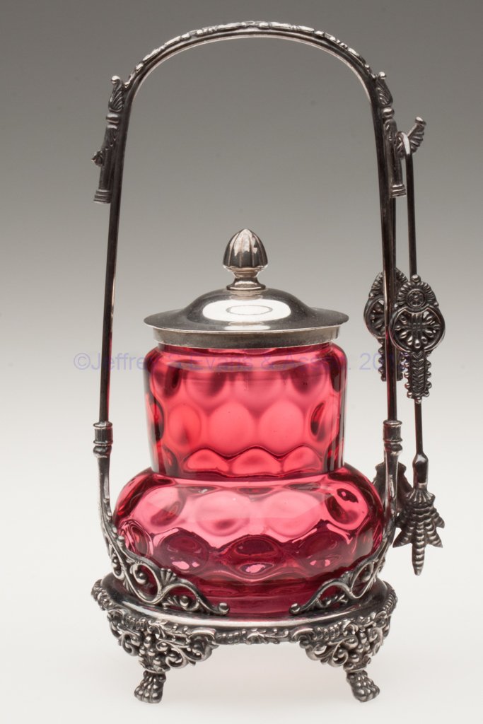 DOT- / SPOT- OPTIC PICKLE CASTER: DOT- / SPOT- OPTIC PICKLE CASTER, cranberry, Van Bergh #610 quadruple-plate stand with tongs. Fourth quarter 19th century. 9 3/4" HOA, 4 1/4" H jar. Provenance: From the collection of the late Marjori
