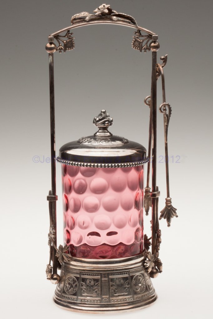 DOT- / SPOT-OPTIC PICKLE CASTER: DOT- / SPOT-OPTIC PICKLE CASTER, cranberry, Rogers & Bro. #206 triple-plate stand with tongs. Fourth quarter 19th century. 12" HOA, 4 1/2" H jar. Provenance: From the collection of the late Marjorie H
