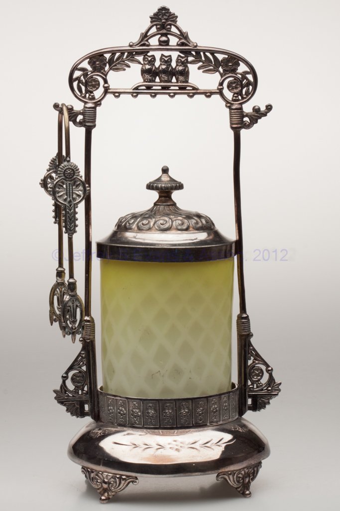 MOTHER-OF-PEARL SATIN PICKLE CASTER: MOTHER-OF-PEARL SATIN PICKLE CASTER, opal cased shaded yellow with diamond air traps, polished pontil mark, illegibly marked (probably Derby) quadruple-plate stand with three owls on handle and tongs.