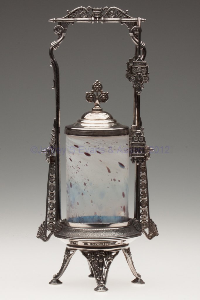 STUDIO GLASS PICKLE CASTER: STUDIO GLASS PICKLE CASTER, swirling opal with amethyst oil spots, rough pontil mark, unmarked quadruple-plate stand with deer heads and tongs. Stand fourth quarter 19th century. Jar 20th century. 13 