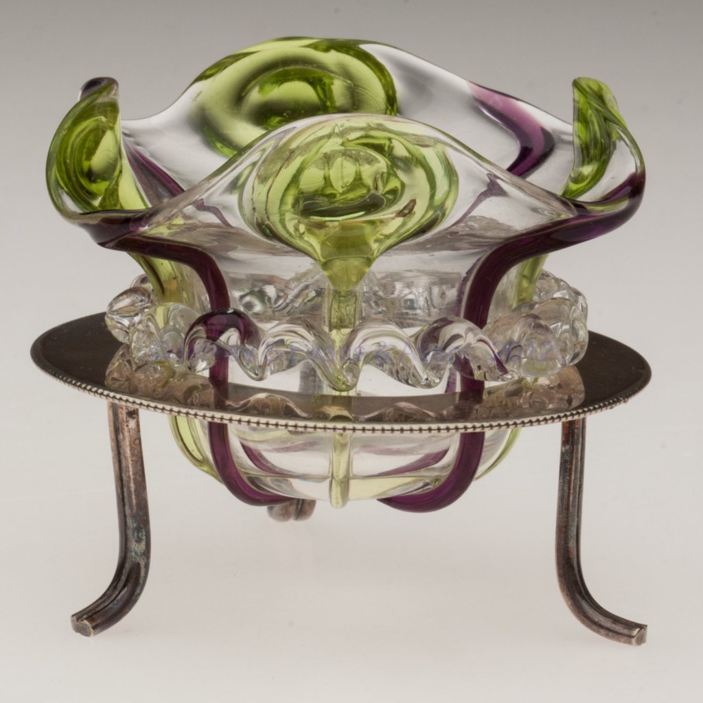 LILY-PAD DECORATED OPEN SALT: LILY-PAD DECORATED OPEN SALT, colorless with applied green lily-pad and amethyst ribs, additional applied colorless rigaree, polished pontil mark, fitted in a "D&A / EPNS" stand with three feet. Late 