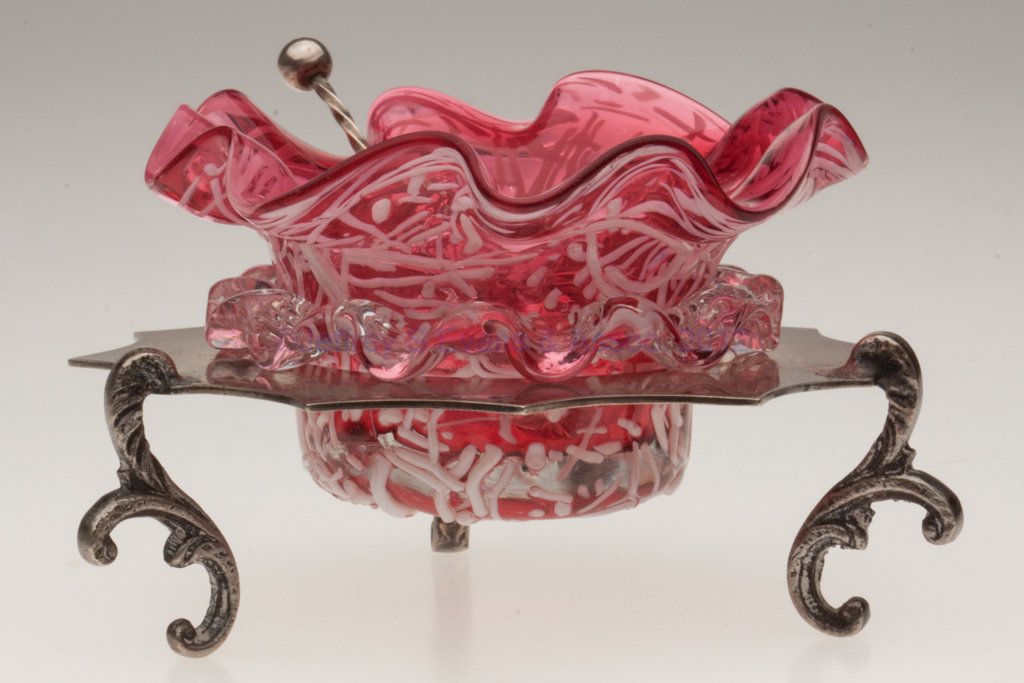 PELOTON DECORATED OPEN SALT: PELOTON DECORATED OPEN SALT, cranberry with opal canes and applied colorless rigaree, polished pontil mark, fitted in an unmarked silver-plate stand with four feet, unmarked spoon. Probably Thomas Web
