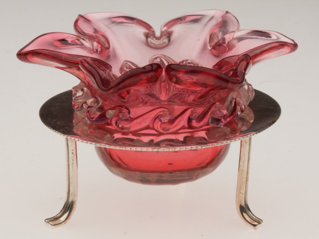 RIB-OPTIC OPEN SALT: RIB-OPTIC OPEN SALT, cranberry with applied colorless rigaree, six-petal flower form, polished pontil mark, fitted in a "D&A / EPNS" stand with three feet. Probably Thomas Webb & Sons, England. Late 1