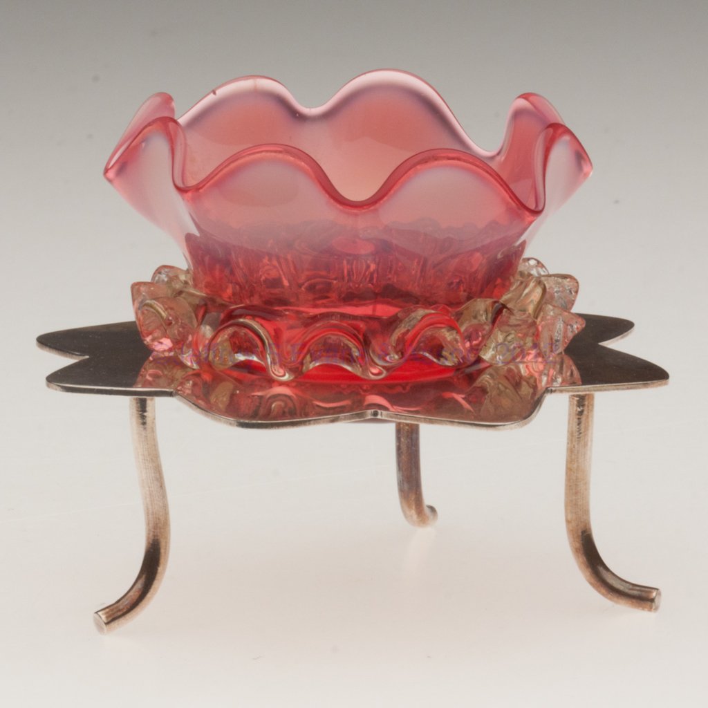 RIB-OPTIC OPEN SALT: RIB-OPTIC OPEN SALT, cranberry opalescent with applied vaseline (uranium) rigaree, polished pontil mark, fitted in a "K & Co. D" silver-plated stand with three feet. Late 19th/early 20th century. 3" H