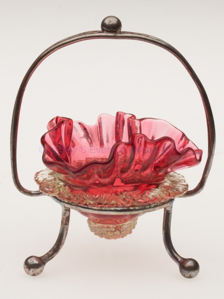 TWO-COLOR OPEN SALT: TWO-COLOR OPEN SALT, cranberry with applied vaseline (uranium) rigaree and berry prunt, crimped triangular rim, fitted in an unmarked silver-plate stand with handle and three feet. Late 19th/early 20t