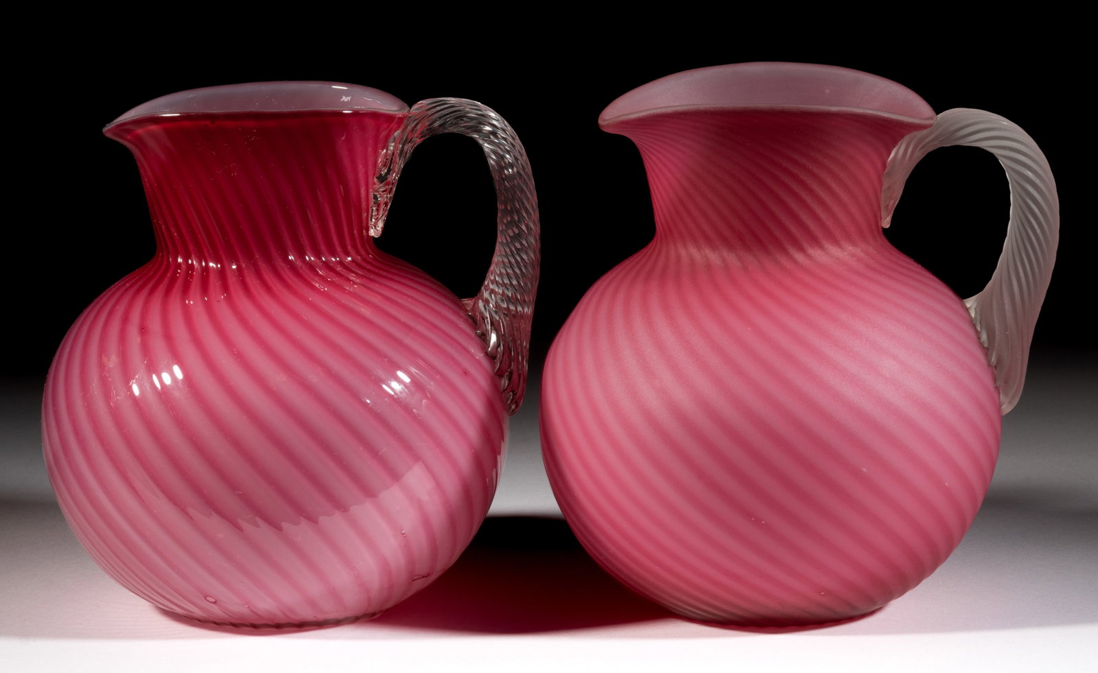 HOBBS NO. 230 / NEAPOLITAN NO. 5 JUG / WATER PITCHERS, LOT OF TWO: HOBBS NO. 230 / NEAPOLITAN NO. 5 JUG / WATER PITCHERS, LOT OF TWO, pink (ruby plated over colorless), glossy and plush, each having swirled optic ribs, an ovoid rim, and applied colorless reeded handl