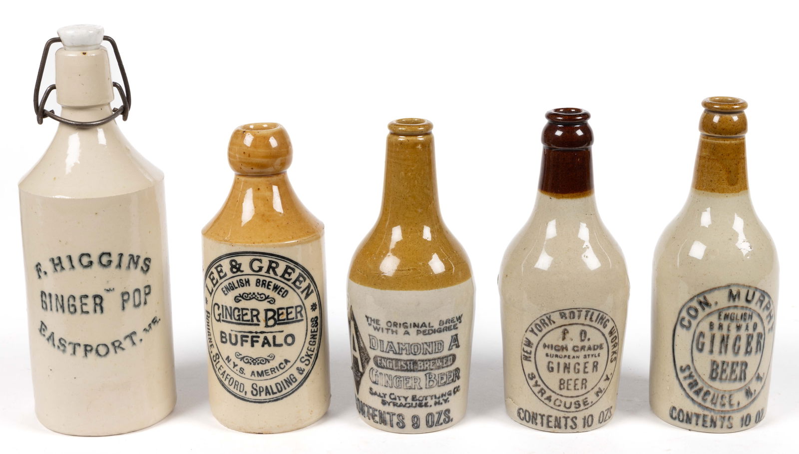 NEW YORK AND NEW ENGLAND STONEWARE GINGER BEER BOTTLES, LOT OF FIVE: NEW YORK AND NEW ENGLAND STONEWARE GINGER BEER BOTTLES, LOT OF FIVE, Bristol-slip coated surfaces mostly with brown or tan shoulders/necks, with black ink stamps, comprising two Syracuse NY "