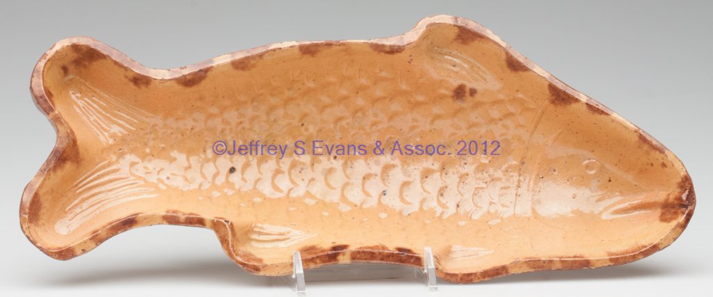 AMERICAN EARTHENWARE FIGURAL FOOD MOLD: AMERICAN EARTHENWARE FIGURAL FOOD MOLD, lead and manganese glazes over a yellow slip wash, fish form with scales and fins, raised on two tab-like feet. Second half 19th century. 2 1/2" H, 5 1/2" x 13