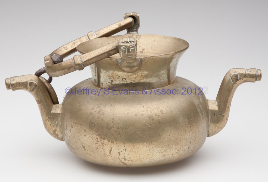 EUROPEAN BRONZE DOUBLE-SPOUT HEARTH KETTLE: EUROPEAN BRONZE DOUBLE-SPOUT HEARTH KETTLE, bail handle with swivel hanging ring, the handle supports of human-head form and the spouts of dog-head form. 17th or 18th century. 12 1/2" HOA, 5 1/4" H ri