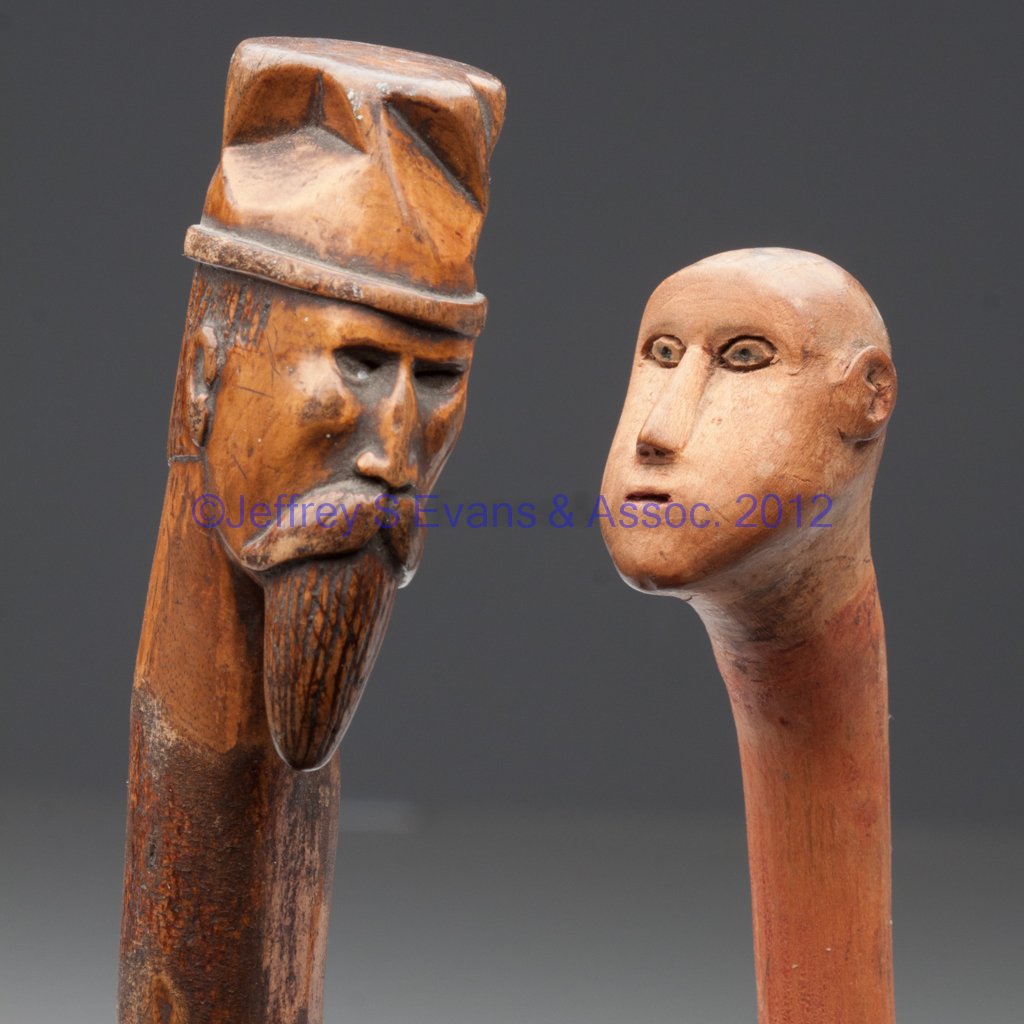 VIRGINIA CARVED FOLK ART WALKING STICKS, LOT OF TW: VIRGINIA CARVED FOLK ART WALKING STICKS, LOT OF TWO, each with a full head for handle, one wearing a hat and with a large mustache and long beard. Original natural surfaces, one with a light red wash.