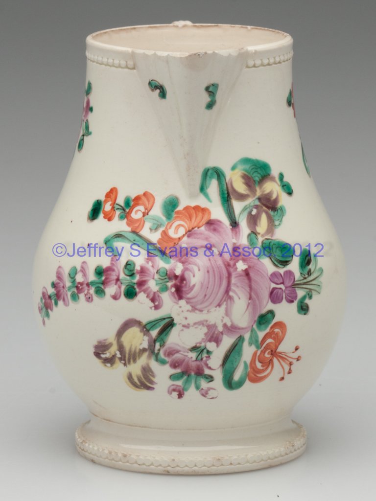 ENGLISH CREAMWARE FOOTED CREAM JUG: ENGLISH CREAMWARE FOOTED CREAM JUG, ribbed spout and a moulded band of beading under the rim and before the edge of the foot, with strap-moulded, entwined handles terminating in appliqué floral sprig