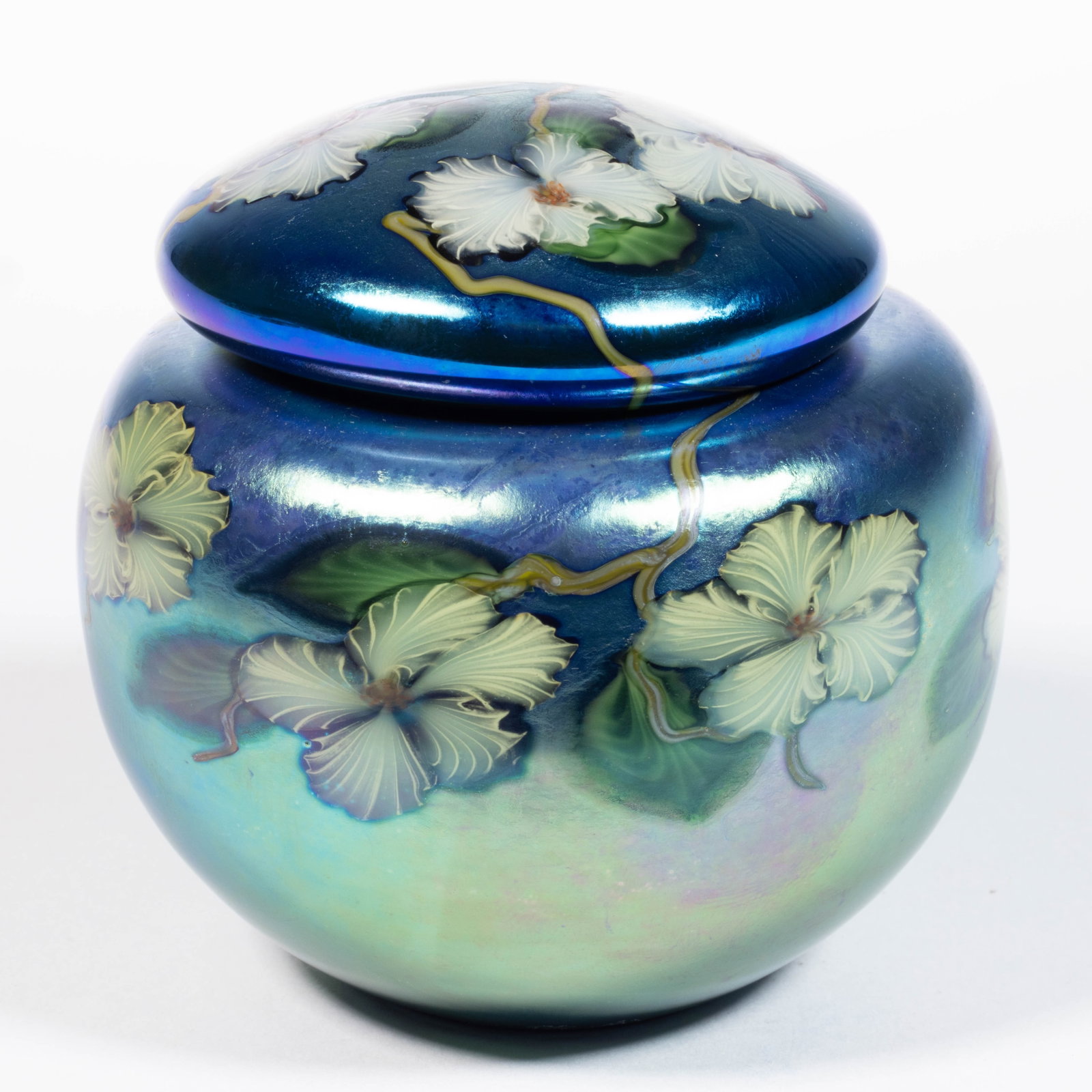 LUNDBERG STUDIOS FLOWERING VINE IRIDESCENT STUDIO ART GLASS COVERED JAR: LUNDBERG STUDIOS FLOWERING VINE IRIDESCENT STUDIO ART GLASS COVERED JAR, blue iridescent, six white flowers to the base and five to the cover, each supported by a brown branch with green leaves, signe