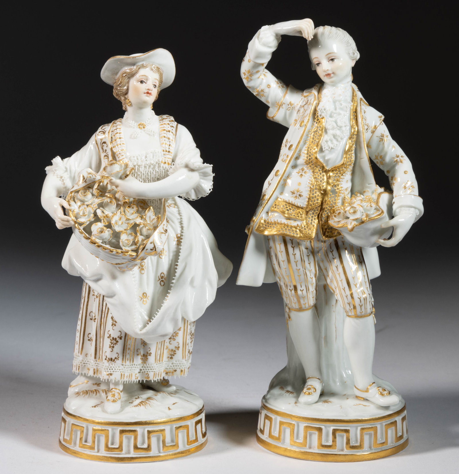 GERMAN MEISSEN PORCELAIN PAIR OF FIGURES: GERMAN MEISSEN PORCELAIN PAIR OF FIGURES, each standing on a circular base and having gilt decorations, comprising a woman holding a basket of flowers and a gentleman holding a hat full of flowers.&nb