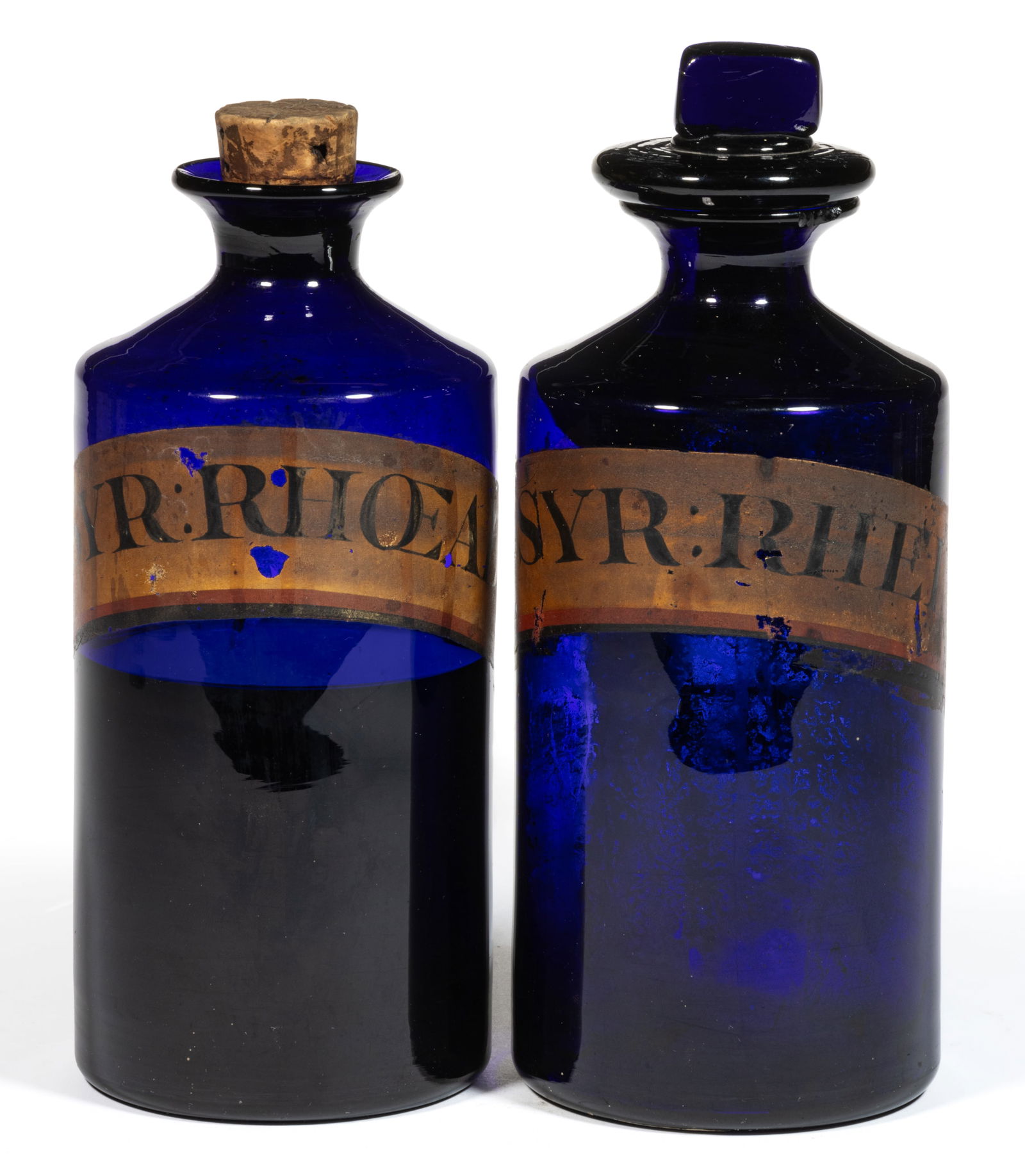 FREE-BLOWN GLASS APOTHECARY BOTTLES / JARS, LOT OF TWO: FREE-BLOWN GLASS APOTHECARY BOTTLES / JARS, LOT OF TWO, cobalt blue, cylindrical forms with short necks and flaring tooled mouths, painted labels below shoulders identifying contents as "SYR:RHEI