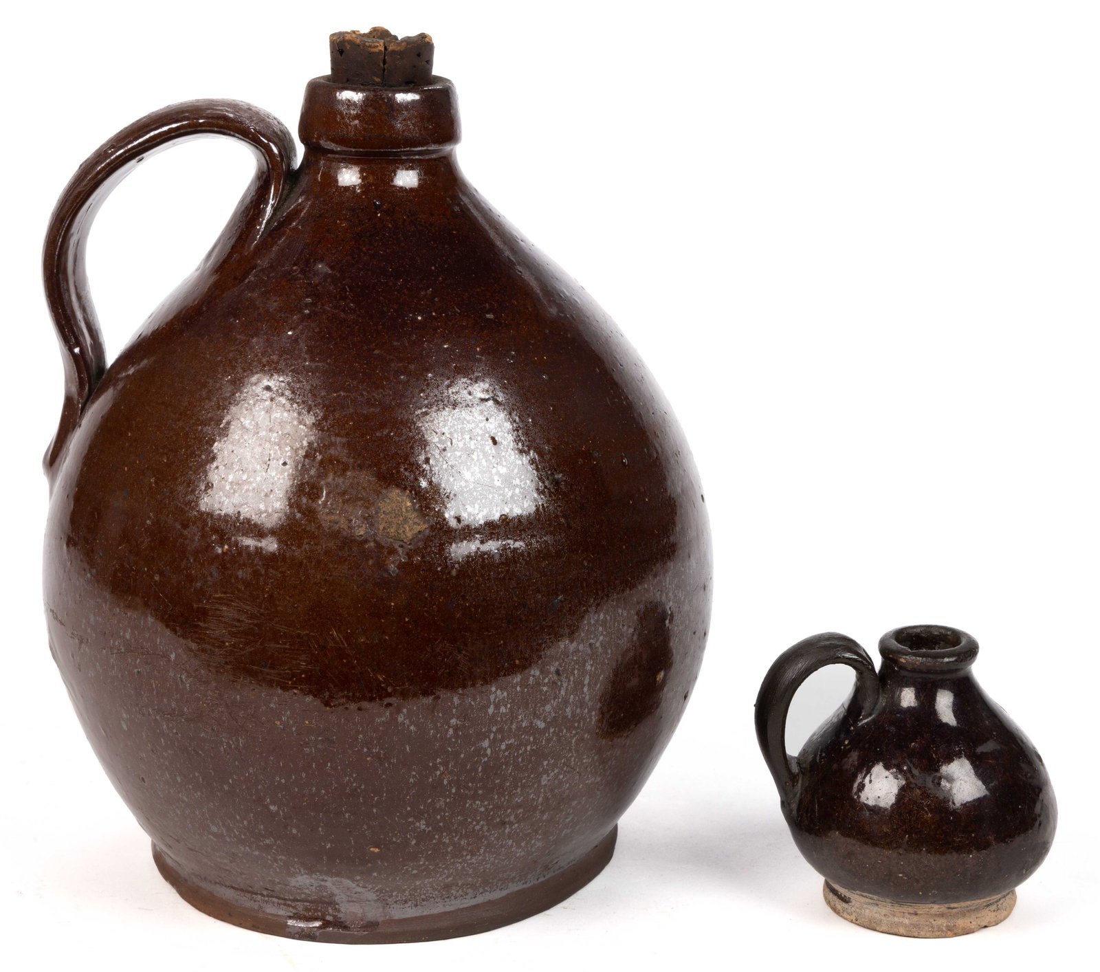 AMERICAN EARTHENWARE / REDWARE JUGS, LOT OF TWO: AMERICAN EARTHENWARE / REDWARE JUGS, LOT OF TWO, lead-glazed to just above foot, bulbous ovoid form with applied strap handles, comprising a miniature example and an approximately half-gallon cap