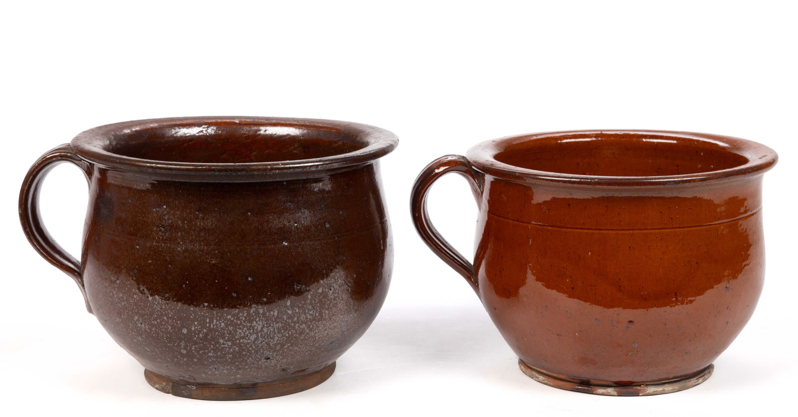 AMERICAN EARTHENWARE / REDWARE CHAMBER POTS, LOT OF TWO: AMERICAN EARTHENWARE / REDWARE CHAMBER POTS, LOT OF TWO, lead-glazed to foot, squat wide-mouth form with flat-top rim and applied strap handle with medial groove. 19th century. 6 7/8" HOA. P