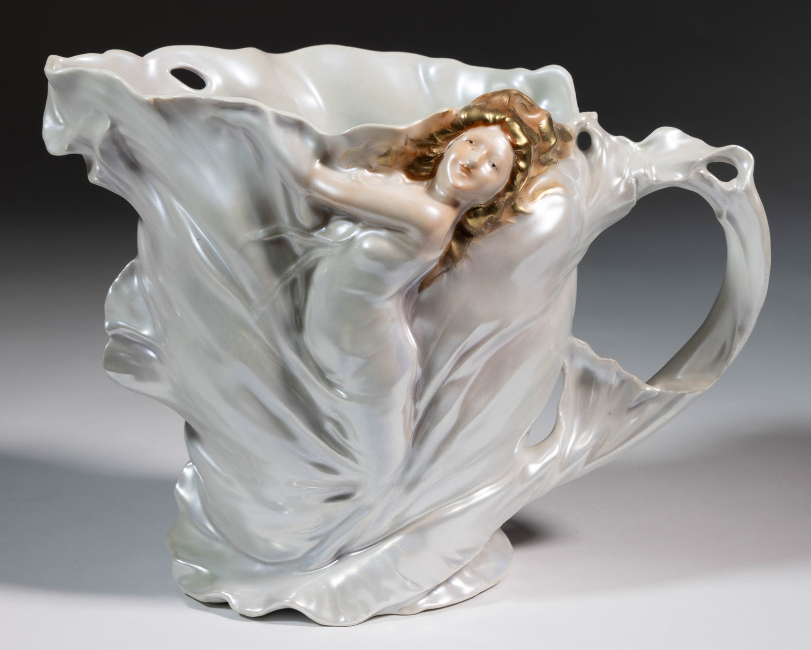 GERMAN ROYAL BAYREUTH PORCELAIN FIGURAL ART NOUVEAU LADY WATER JUG / PITCHER: GERMAN ROYAL BAYREUTH PORCELAIN FIGURAL ART NOUVEAU LADY WATER JUG / PITCHER, depicting a central molded image of a woman with gold-accented brown hair and dressed in flowing material with iridescent 