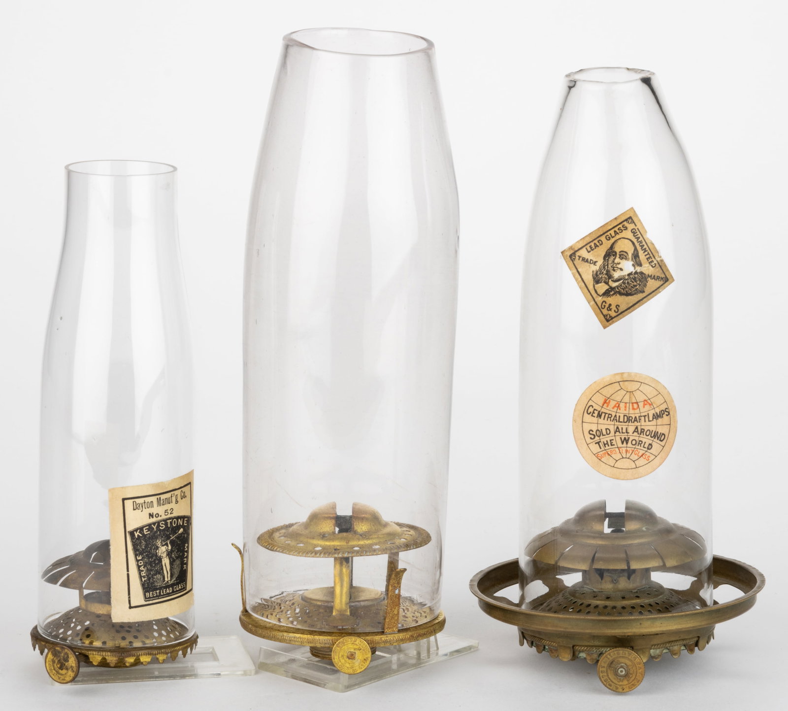 ASSORTED COLLINS AND SIMILAR SLIP BURNER AND CHIMNEY SETUPS, LOT OF THREE: ASSORTED COLLINS AND SIMILAR SLIP BURNER AND CHIMNEY SETUPS, LOT OF THREE, brass, includes a No. 0 and a No. 1 Collins, each with thumbwheels marked with patent dates, No. 1 example fitted with a 3 1/