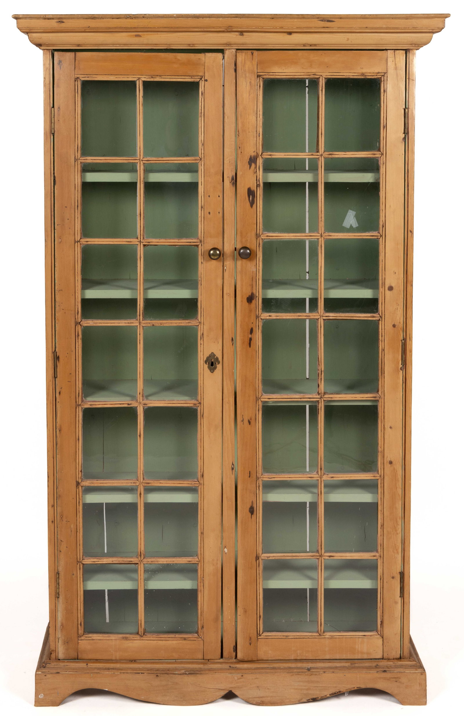 COUNTRY PINE DISPLAY CABINET: COUNTRY PINE DISPLAY CABINET, the molded cornice over two 14-pane cabinet doors, each with a brass knob, which conceal a painted interior with five fixed shelves, the whole supported by an applied bra