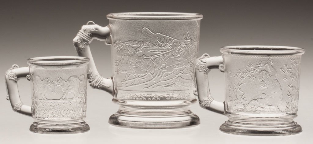 CRYSTALLOGRAPHY CHILDREN'S GLASS MUGS, LOT OF THRE: CRYSTALLOGRAPHY CHILDREN'S GLASS MUGS, LOT OF THREE, colorless, comprising Fighting Cats, Monkeys and Vines and Santa Claus examples. Late 19th/early 20th century. 2 1/4" to 3 1/2" H. Provenance: The 
