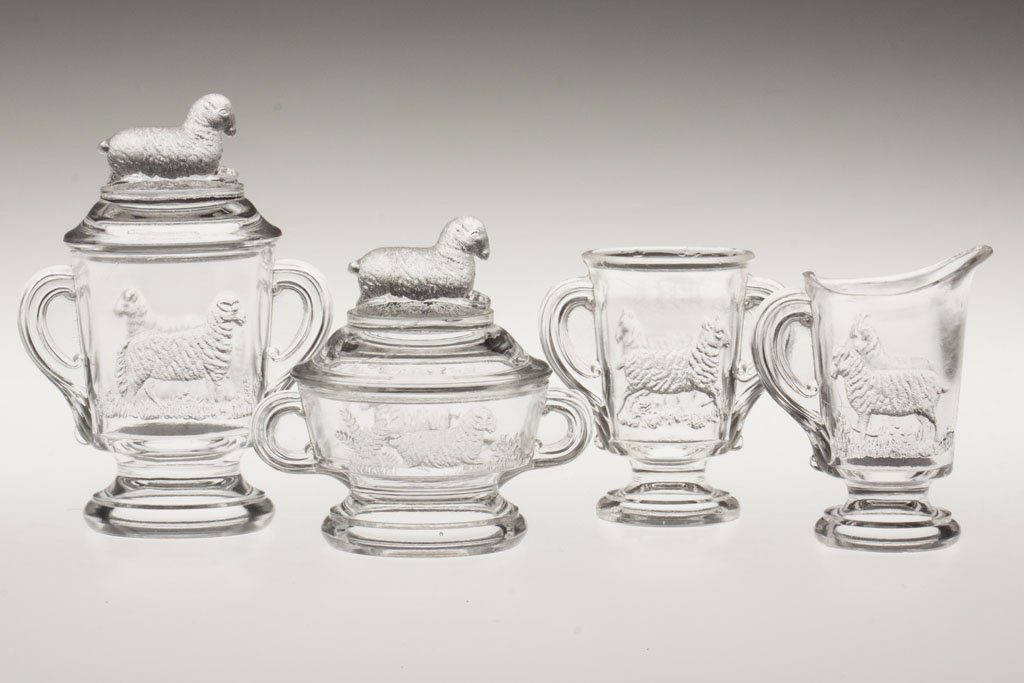 LAMB CHILDREN'S GLASS FOUR-PIECE TABLE SET: LAMB CHILDREN'S GLASS FOUR-PIECE TABLE SET, colorless, comprising a covered butter dish, covered sugar bowl, creamer and spooner. Early 20th century. 3 1/8" to 4 1/4" HOA. Provenance: The collection o