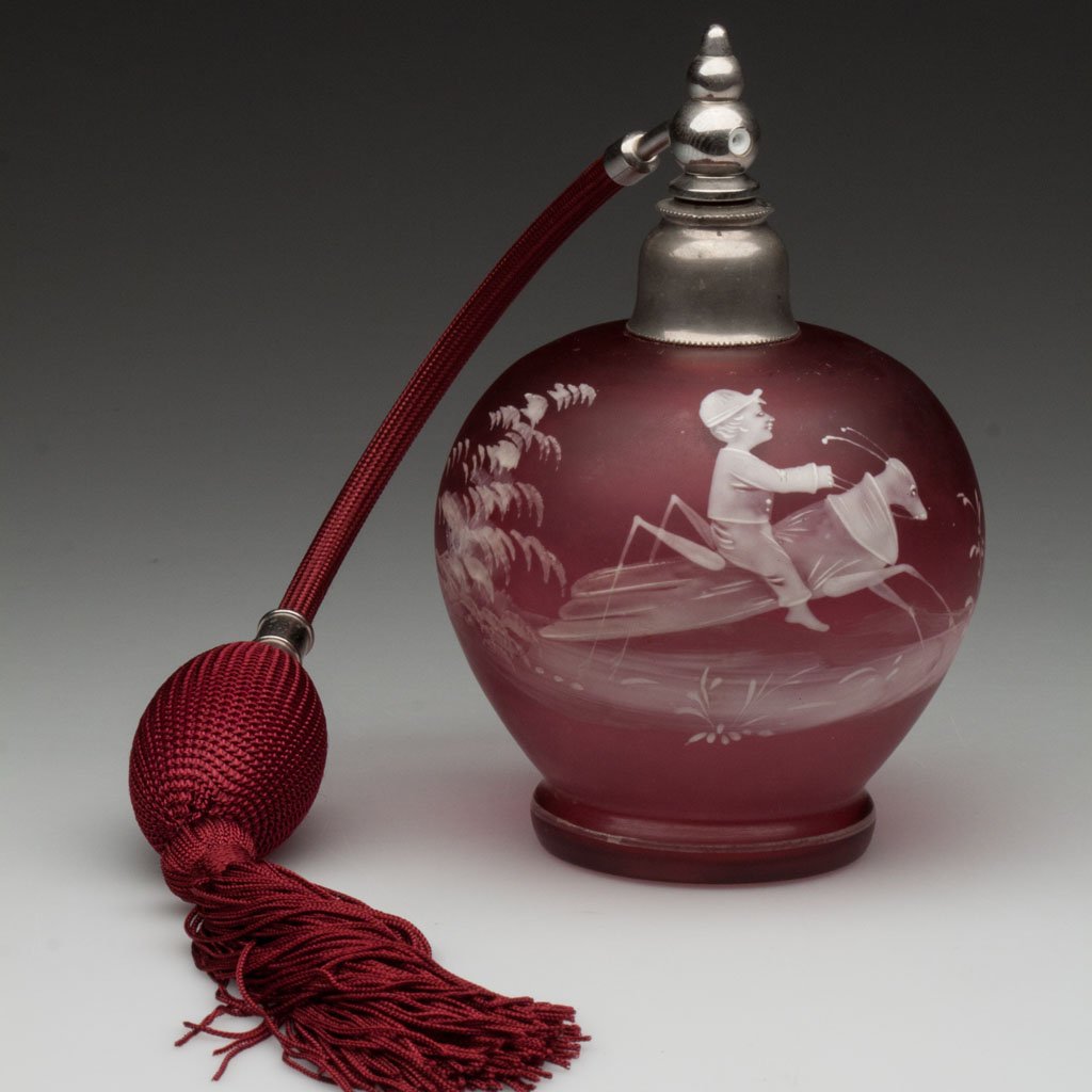 MARY GREGORY (SO CALLED) ATOMIZER: MARY GREGORY (SO CALLED) ATOMIZER, cranberry, satin finish, white enamel decoration featuring a boy riding a grasshopper, metal mount, replaced fabric and bulb. Late 19th/early 20th century. 5 1/2" H.