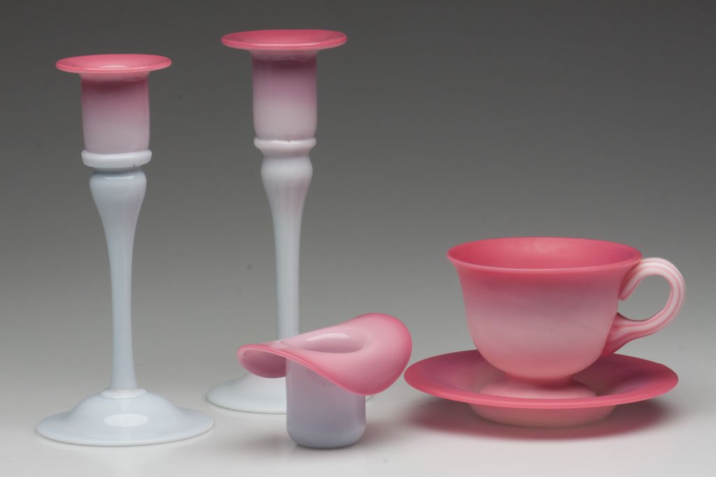 PAIRPOINT PEACHBLOW ARTICLES, LOT OF FIVE: PAIRPOINT PEACHBLOW ARTICLES, LOT OF FIVE, comprising two glossy Breyden candlesticks and a hat-form whimsy, and a plush Gunderson cup and saucer. Second half 20th century. 2" to 6 3/4" H. Provenance: