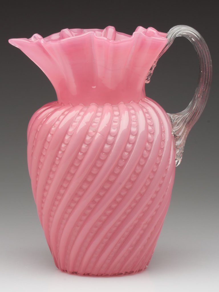 VICTORIAN CASED GLASS WATER PITCHER: VICTORIAN CASED GLASS WATER PITCHER, cased pink, swirls with beads pattern, star-form crimped rim, colorless applied reeded handle, polished pontil mark. Late 19th/early 20th century. 9 3/8" HOA.